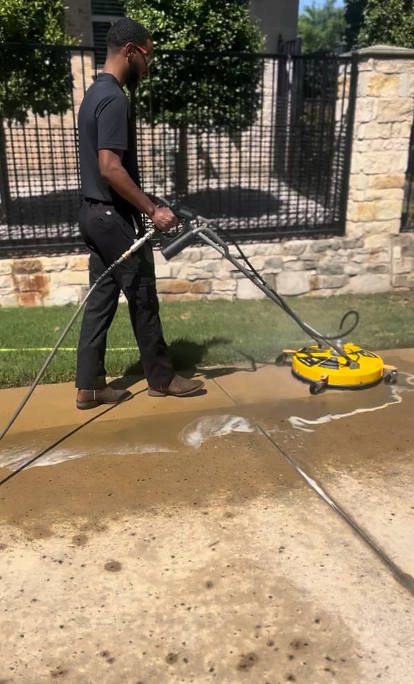 A technician pressure washing a concrete driveway with a surface cleaner