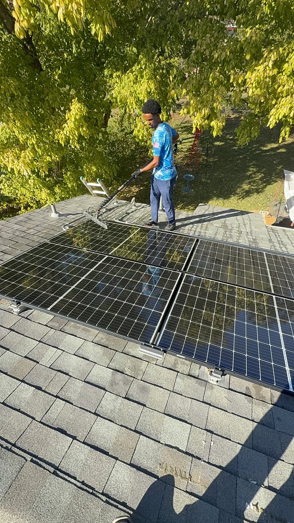 A technician on a roof cleaning a solar panel array