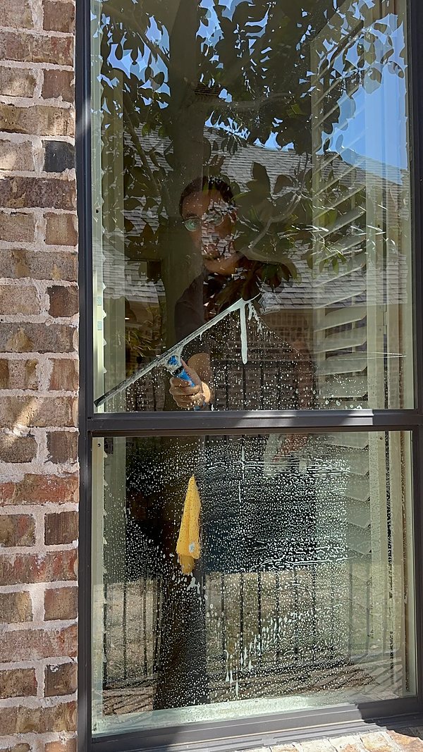A technician inside the house squeegeeing a soaped window pane